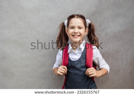 Cheerful schoolgirl with a backpack and school uniform on a gray background, back to school, copy space.