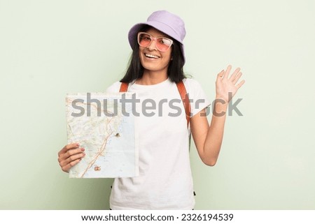 young pretty hispanic woman smiling happily, waving hand, welcoming and greeting you tourist and map concept Royalty-Free Stock Photo #2326194539