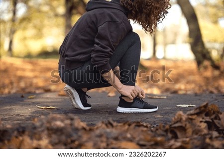 Woman in sports clothes tying shoes before jogging in the park Royalty-Free Stock Photo #2326202267