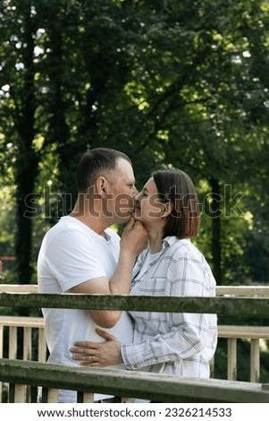 A portrait of a young beautiful Caucasian couple standing and kissing on the lips in love on an old wooden bridge over a brook in the park on a summer day..