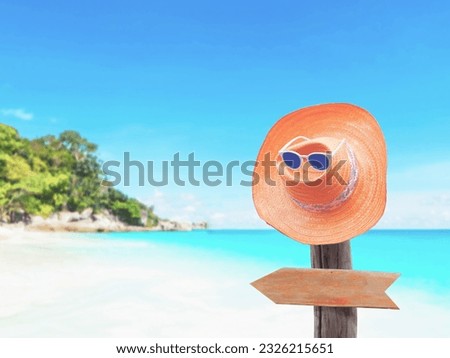 Vintage straw hat and blank brown wooden board arrow shape hanging on wood post over summer beach background. Happy holiday concept.