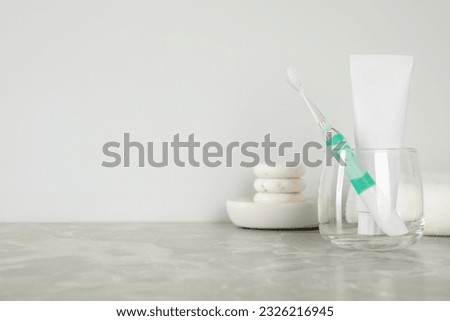Electric toothbrush in glass and tube with paste on light grey marble table. Space for text