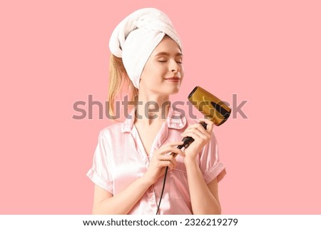 Young woman in towel with hair dryer on pink background Royalty-Free Stock Photo #2326219279