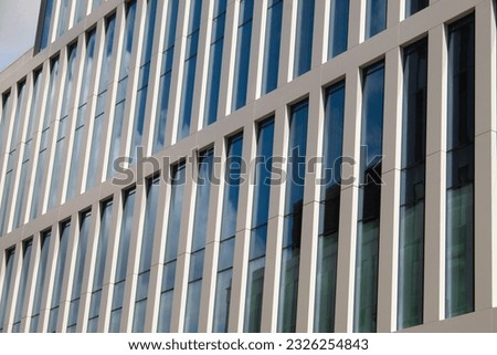 A vertical facade of white metal panels, high windows reflecting the sky. Modern did architecture.