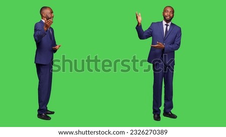 Businessman in office suit pointing sideways on camera, creating corporate presentation over full body greenscreen backdrop. Young male employee showing advertisement in studio.