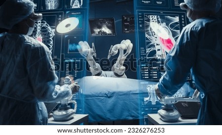 Surgeons Wearing AR Headsets And Using High-Precision Remote Controlled Robot Arms To Operate On Patient In Hospital. Doctors Working With Robotic Limbs, Observing Vitals On Holographic VFX Displays. Royalty-Free Stock Photo #2326276253