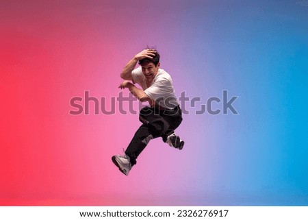 male dancer jumps and flies in the air, young guy hiphop performer break dances in neon club lighting and does acrobatic stunt