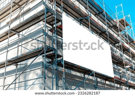Blank white advertisement hanging on the scaffolding of modern building under construction.Reconstruction of a building with white billboard.