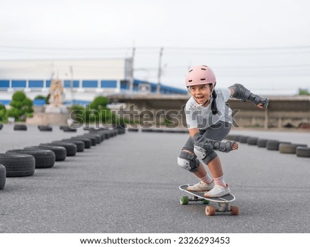 asian child skater or kid girl fun playing skateboard or smile riding carving surf skate on car tires track in skate park lane for extreme sports exercise and wears helmet knee guard for body safety Royalty-Free Stock Photo #2326293453