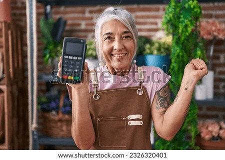 Middle age woman with tattoos working at florist shop holding dataphone screaming proud, celebrating victory and success very excited with raised arm 