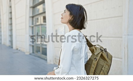 Young beautiful hispanic woman tourist wearing backpack standing at street