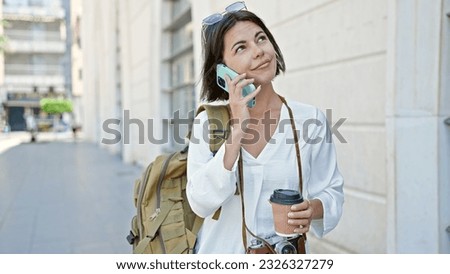 Young beautiful hispanic woman tourist talking on smartphone drinking coffee at street