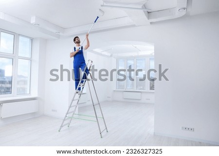 Handyman painting ceiling with roller on step ladder in room Royalty-Free Stock Photo #2326327325