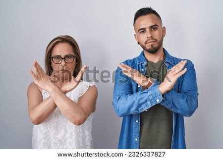 Hispanic mother and son standing together rejection expression crossing arms doing negative sign, angry face 
