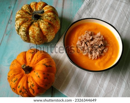on a blue wooden table there is a gray round plate of pumpkin cream soup with tuna next to two small pumpkins.  gluten-free, vegan.  diet.  view from above.  menu calendar