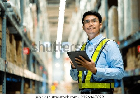 warehouse worker in a blue security suit uses a digital tablet to inspect inventory in a large warehouse. Distribution Center. Logistics and export of business.
