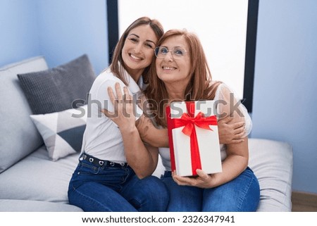 Mother and daughter surprise with gift hugging each other at home