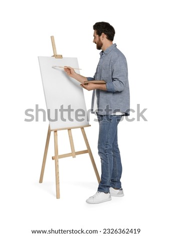Man with brush painting against white background. Using easel to hold canvas