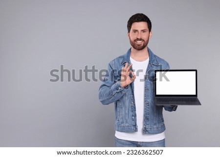 Happy man with laptop showing ok gesture on light grey background. Space for text
