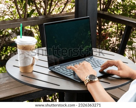 With a cup of coffee beside her, a young woman's hand elegantly navigates the laptop, indulging in the convenience and excitement of online shopping, as she explores a world of endless possibilities.
