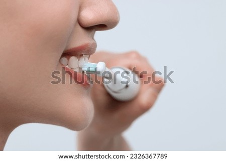 Woman brushing her teeth with electric toothbrush on white background, closeup. Space for text Royalty-Free Stock Photo #2326367789