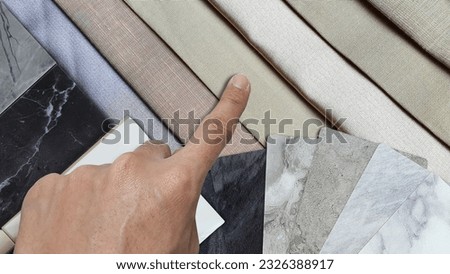 close up of interior architect's hand chooses material samples contains stone ceramic tile, marble artificial stones, marble laminated swatch placed on multi color velvet drapery palette. 