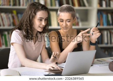 Two positive pretty young student girls studying in college library, working on class project together, practicing teamwork, enjoying higher university education, using laptop computer Royalty-Free Stock Photo #2326389565