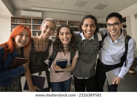 Cheerful high school students enjoying meeting, leisure in campus library, hugging, posing, bending forward, looking at camera with toothy smiles, laughing. Happy university mates portrait