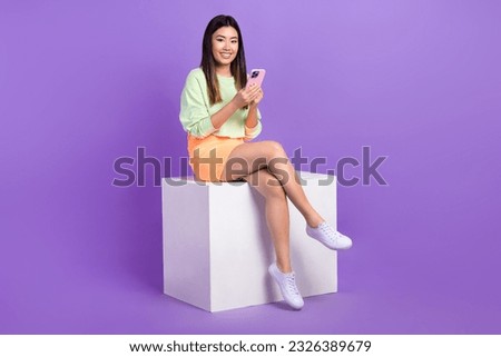 Full size photo of adorable cheerful nice woman sitting on podium read notification in smartphone isolated on purple color background
