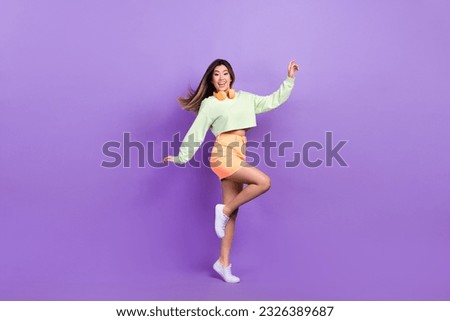 Full size photo of satisfied optimistic pretty woman dressed green shirt stylish skirt stand on tiptoe isolated on purple color background