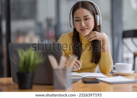 Young adult happy smiling Asian student or business woman wearing headphones talking on online chat meeting using laptop in office or campus, asian female student wear glasses learning remotely.