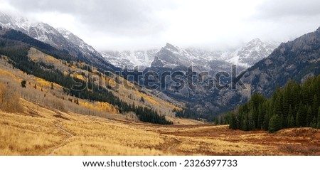 A picture with snow capped mountains in the background and a valley in the foreground