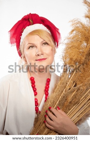 Portrait of heerful funny adult mature woman solokha with sheaf of ears. Female model in clothes of national ethnic Slavic style. Stylized Ukrainian, Belarusian or Russian woman in comic photo shoot