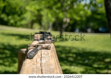 an old large wooden board in a green garden on which stacks of hammers stand