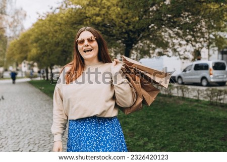 Happy young redhead woman holding shopping paper bags in hands, walking at city street, black friday. Urban lifestyle concept. Shopping banner, for mockup