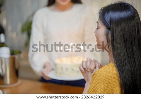 Cheerful friends enjoying home Birthday holiday party. Asian sister cheering drinking red wine celebrating with Birthday cake