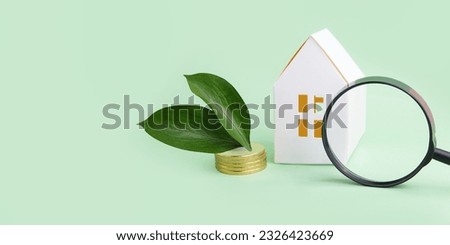 Concept of green tax credit - little house with coins near it, green leafs and magnifying glass.Large banner with negative space.