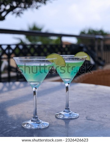 The two cocktails on a table on an outdoor patio.