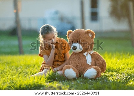 Sad lonely child girl spending time together with her teddy bear friend outdoors on sunny backyard. Loneliness at preteen age Royalty-Free Stock Photo #2326443911
