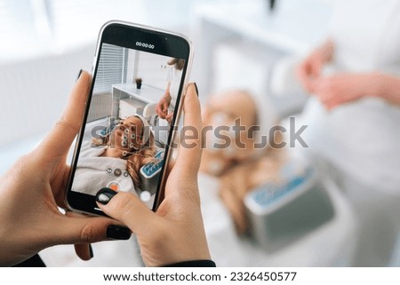Recording video or take photo on phone of hardware electro myostimulation procedure in clinic of aesthetic medicine. Hardware electro myostimulation procedure at beauty spa salon.
