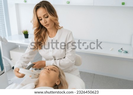 Front view of professional cosmetician performing photo rejuvenation cosmetology procedure for woman in modern cosmetology clinic. Concept of technology hardware for anti age-related changes of face