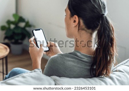 Shot of back view of young woman using mobile phone sitting on a couch at home Royalty-Free Stock Photo #2326453101