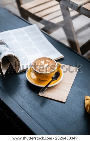 A vertical shot of cappuccino in a yellow coffee cup on the table with a journal