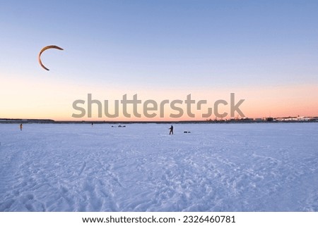 A scenic view of a snow-covered beach with colorful kites flying in the clear blue sky. In the distance, a city skyline glimmers under the sunlight. A perfect image for travel or seasonal themes.