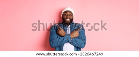 Happy young african-american hipster guy pointing fingers sideways, smiling and showing two choices, showing offers, standing over pink background.