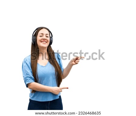 Cute young brunette woman smiling and pointing her fingers to one side while wearing headphones against a white background