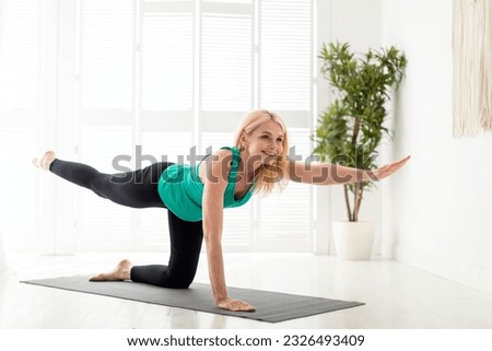 Beautiful mature lady in sportswear doing morning yoga, making bird dog pose, smiling senior woman training on fitness mat at home, stretching opposite leg and arm, enjoying healthy lifestyle Royalty-Free Stock Photo #2326493409