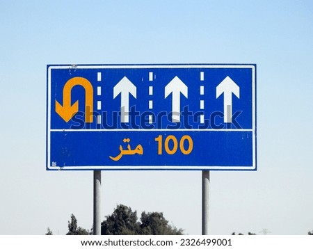  Translation of the Arabic text (100 M one hundred meters) at a side informative traffic sign board showing 4 lanes and directing the drivers for a u turn ahead after 100 meters at the left lane