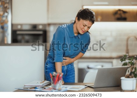 Business woman suffering from stomach ache while working from her home office. Royalty-Free Stock Photo #2326509473