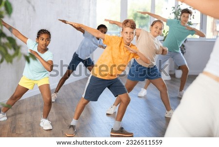 Emotional cheerful tween boy enjoying contemporary dance with group of children, showcasing dabbing move.. Royalty-Free Stock Photo #2326511559